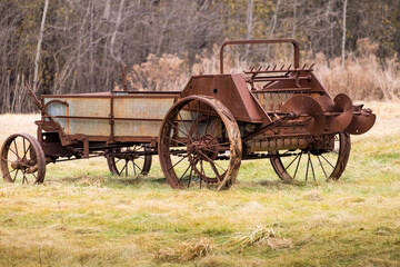 Fototapeta na wymiar An old rusty manure spreader with iron wheels in a field in rural Ontario Canada.