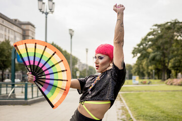 Mexican drag queen with a rainbow fan with her arm up empowered on the streets of Berlin