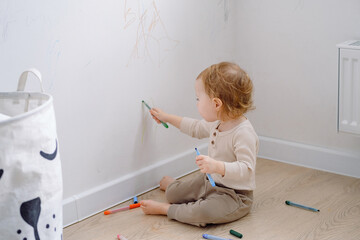 Toddler scribbling on white wall at home. Little kid drawing on walls by colored markers. Art...