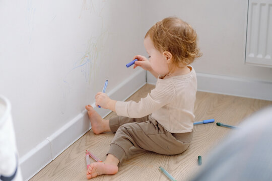 Little kid drawing on walls by colored markers. Toddler scribbling on white wall at home. Art therapy, normal behaviour. 