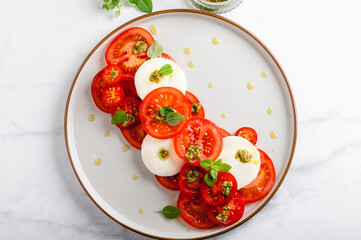 Classic italian salad caprese served in original form with different tomatoes, mozarella, pesto sauce and basil