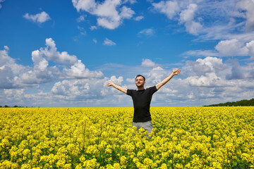 Man stands in a yellow field rejoicing raises his hands to the sky.