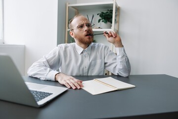 A man wheelchair businessman in the office works at a laptop, writing down ideas and a plan in a notebook, thoughtfulness, integration into society, the concept of working a person with disabilities