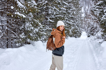 Fototapeta premium Attractive Red-haired Woman In Stylish Warm Coat With Backpack Walking In Wonderful Winter Forest Alone, Outdoors. Healthy Lifestyle, Recreation, Travel, Hiking, Happiness, Adventure Concept