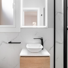 Fototapeta na wymiar Bright bathroom boasts a sleek and minimalist style, featuring a gleaming white sink set against a stunning black framed mirror, creating a modern and sophisticated look.