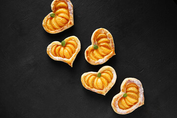 Puff pastry cake in the shape of a heart with tangerine slices and mint leaves on a dark table. top view, copy space