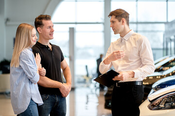 Skilled friendly car seller talking to couple who wants to buy car about performances and...