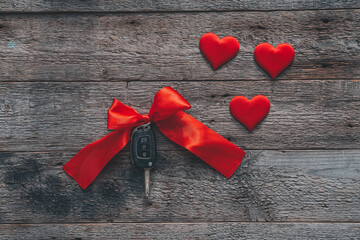 Car keys with red ribbon and heart on wooden background. The concept of a car gift for the holiday of February 14th. Valentine's Day.