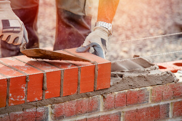 Industrial bricklayer laying bricks on cement mix on construction site - obrazy, fototapety, plakaty