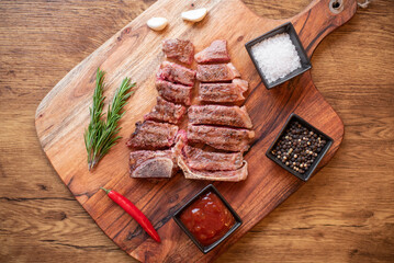 grilled T-bone steak on a cutting board with herbs on a wooden background