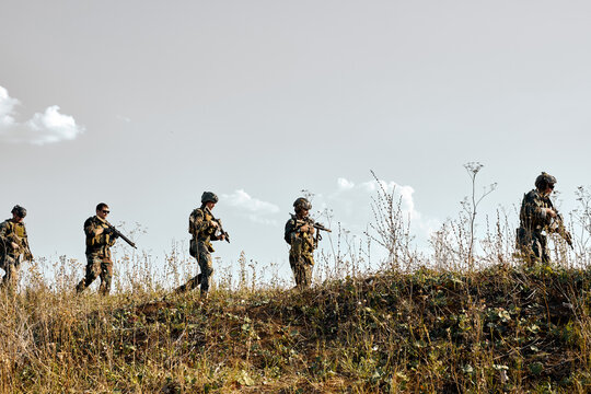 group of brave strong soldiers walking in countryside abandoned area, military training. young armed men in camouflaged uniform going in row.Infantry combat soldiers. military forces
