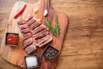 grilled T-bone steak on a cutting board with herbs on a wooden background with copy space for your...