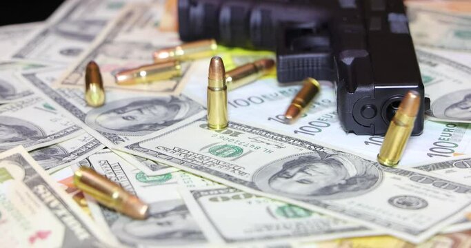 Gun and bullets on dollar and euro banknotes background, closeup shot. Criminal money. Black money and protection, mafia and corruption concept. Bullets fall down, slow motion