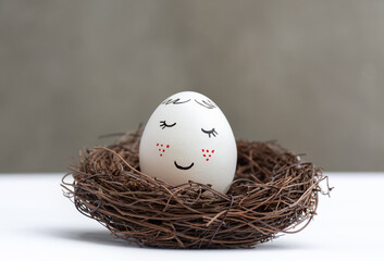 Happy Easter. One white Easter egg in a wicker wooden nest on white table. View is direct. Stylish spring template with copy space
