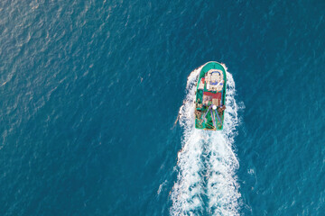 Fishing boat moving on sea surface leaving path of sea foam water. Aerial top view