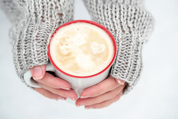 coffee mug, hands, sweater, snow. heart on thick coffee foam. cup in female hands on a background of snow.