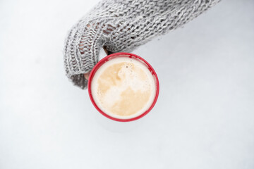 coffee mug, hand, sweater, snow. coffee with thick foam in hand against the background of snow.