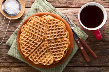 Pile of fresh homemade heart shaped waffles on wooden plate with a cup of tea and powdered sugar on...