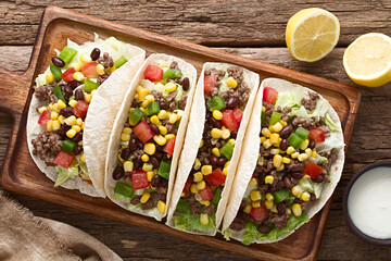 Flour tortillas filled with mincemeat and vegetables, lettuce, tomato, corn, green bell pepper and beans, photographed overhead on wood (Selective Focus, Focus on the tortillas)