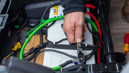 man hand servicing vehicle, tightening battery terminal with tool in hand.