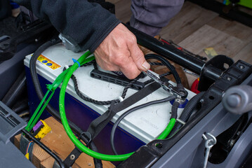 man hand servicing vehicle, tightening battery terminal with tool in hand.