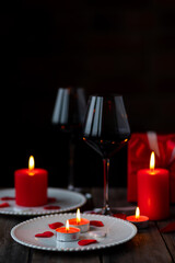 Saint Valentine's Day celebration. Red burning candles, hearts, gift box, postcard on dark wooden background. Happy holiday . Table decor for festive dinner, romantic atmosphere. Copy space for text