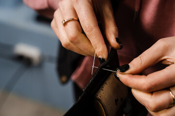 Obraz na płótnie Canvas Craftsman sews genuine leather using needle and thread for creation natural leather products. Equipment for genuine leather production in workshop. Process of stitching genuine leather.