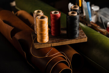 Needle with spools of thread on roll of brown genuine leather in craftsman workshop. Handmade...