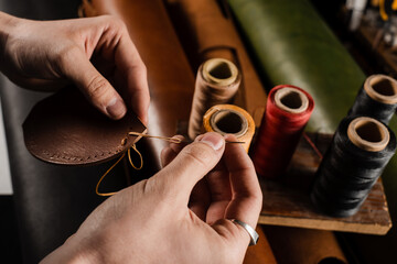 Craftsman sews genuine leather using needle and thread for creation natural leather products....