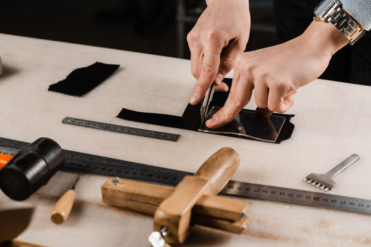 Craftsman is cutting genuine leather using cutter knife for creation natural leather products. Equipment for genuine leather production in workshop. Process of cutting genuine leather.