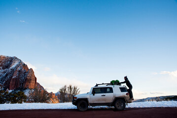 Side view of man putting backpack on off-road vehicle at desert against sky during winter