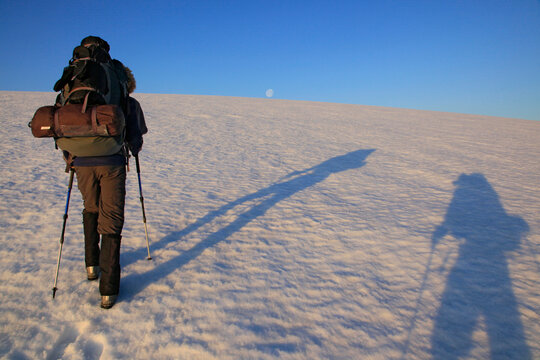 Hikers crossing Drangaj&iuml;&frac34;&scaron;kull ice cap, Hornstrandir Peninsula, Iceland with simultaneous sunrise shadows and full moon