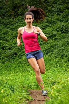 Woman trail running through a green meadow in the woods.