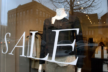 A woman's boutique window display advertises a sale