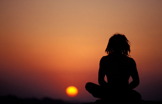 A silhouette of a man meditating at sunset.