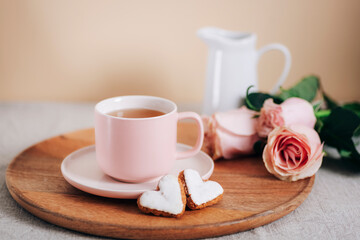 A cup of tea, heart-shaped cookies, pink roses and jug with milk on a wooden tray. Valentines day concept. Morning breakfast. Close up