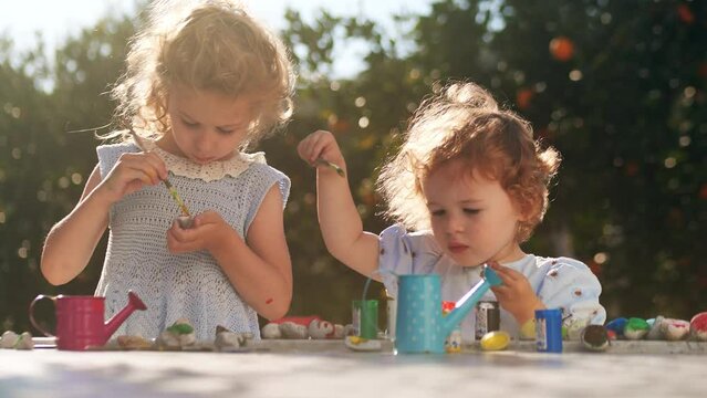 Two adorable little girls paint something on stones in the orange garden together