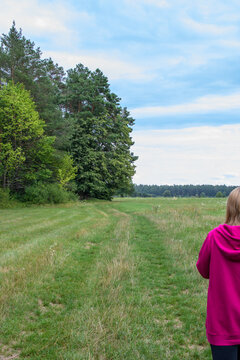 Dziewczyna w r&oacute;żowej bluzie idąca polną ścieżką na skraju lasu