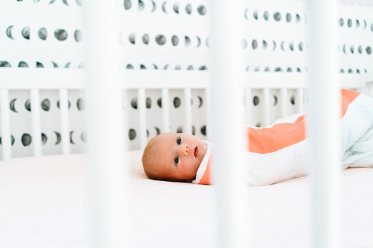 View through a crib of a newborn baby girl laying down