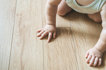 Baby sits on a wooden laminate floor. Bare hands a baby in the living room floor