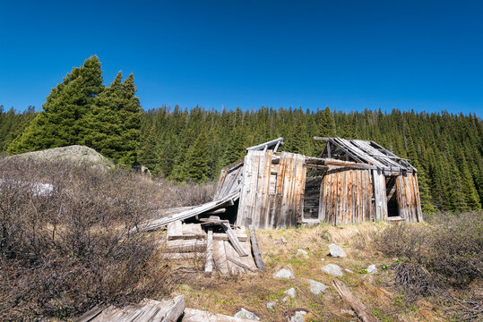 Low angle view of abandoned log cabin against clear blue sky