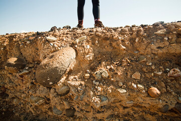A girl stands on the edge of an eroding mesa bluff, with stones and soil exposed, in the badlands of Utah.