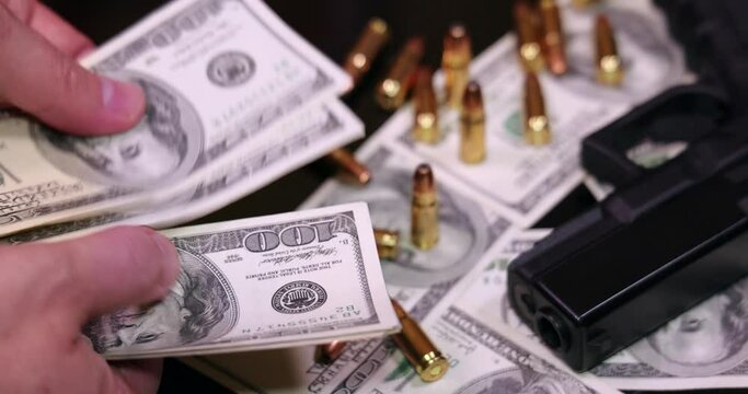 Gun and bullets on dollar banknotes background, closeup shot. Criminal money. Black money and protection, mafia and corruption concept. Male hands count money or pay, slow motion
