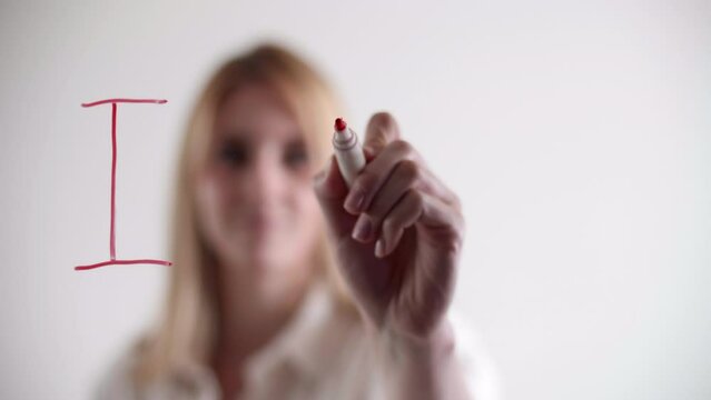 Blonde, caucasian girl uses red marker on a window surface. Close-up view of a beautiful woman writing a love confession on a glass board. High quality 4k footage