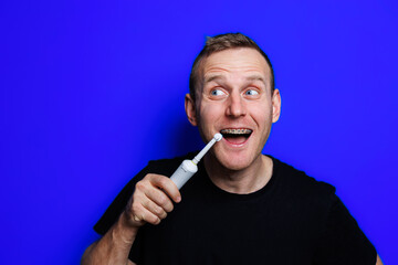 Portrait of a young handsome man brushing his teeth with an ultrasonic modern toothbrush. Oral care. Morning self care