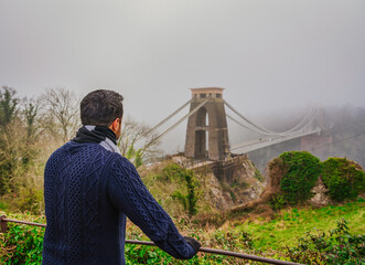 Man looking at famous Clifton bridge in Bristol England on a fog day