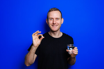 A young man in a black T-shirt on a blue background stands with a thermometer in his hands. An...