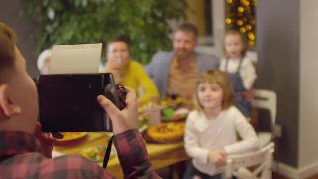Boy taking one polaroid shot of his family and showing it to them