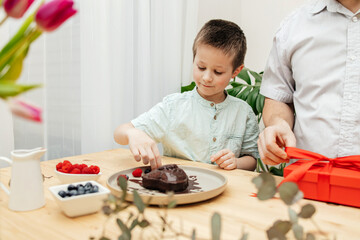 Dad and son decorate a heart-shaped cake with fresh berries and prepare a gift. Mother's Day, International Women's Day, Valentine's Day