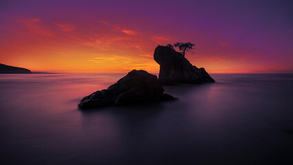 View of wooded rock of bartin inkumu beach with a long exposure low light photo, selective low exposure and saturated sunset colors at horizon